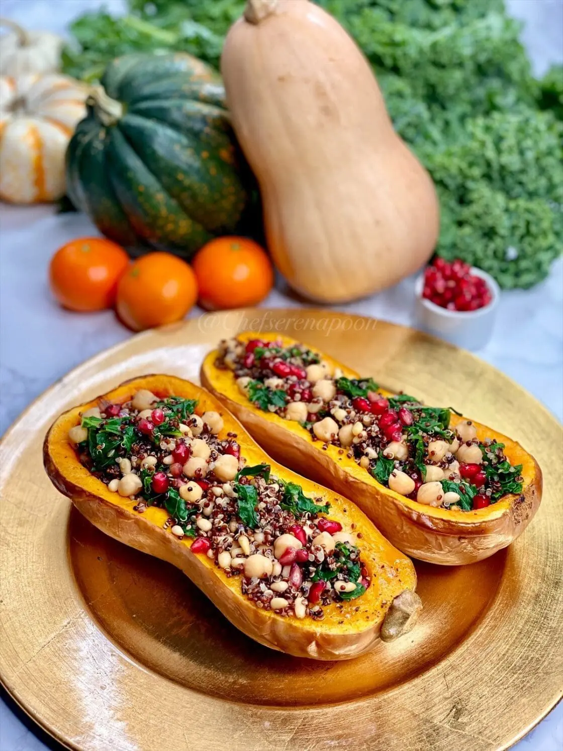 vegetarian stuffed butternut squash on a gold charger with clementines, squash, pomegranate arils, and kale in the backgroud.
