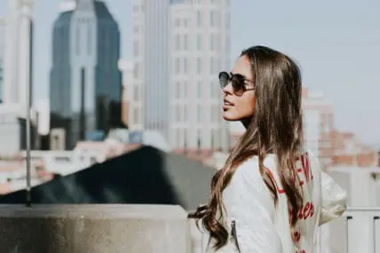 woman with beautiful skin in a jacket wearing sunglasses standing on top of a building looking over her left shoulder. Is taking probiotics for skin the secret to her healthy skin?