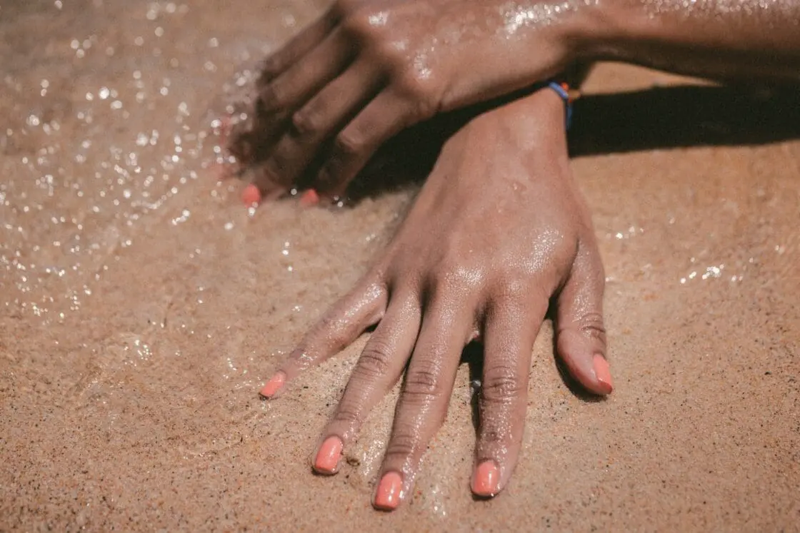 Image of hands with painted nails in ocean sand with smooth skin. Vegan collagen support may help your skin, joints and overall health.