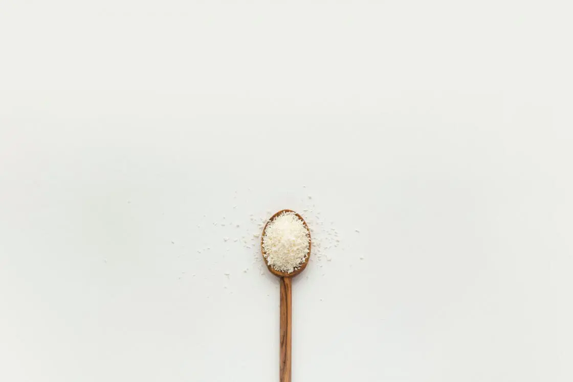 white powder in a wooden spoon. collagen powders are white and used to support skin, hair, joint and nail health.