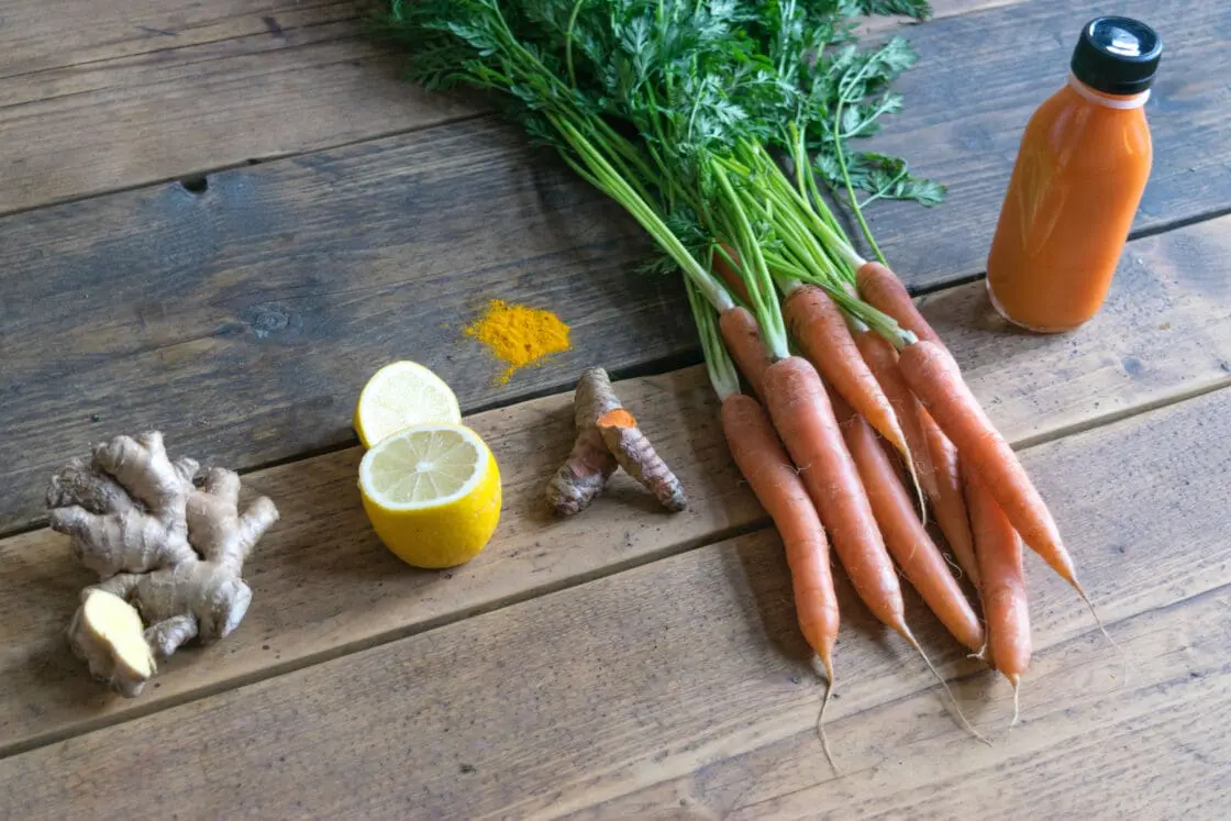 image of orange-colored juice and its ingredients: carrots, ginger, lemon, and turmeric made for juicing cleanse via organic authority.