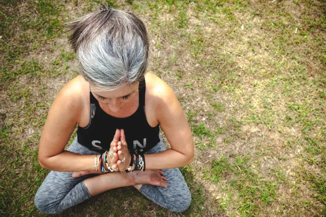 Image of woman doing yoga on grass with gray hair. Vegan collagen support can be used by women of all ages.