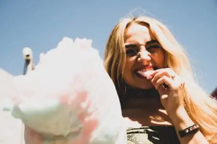 young woman eating cotton candy with sugar that can trigger food intolerances.