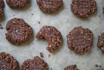 Image of a dozen no bake peanut butter cookies on a parchment lined baking sheet, one with a bite taken out of it.