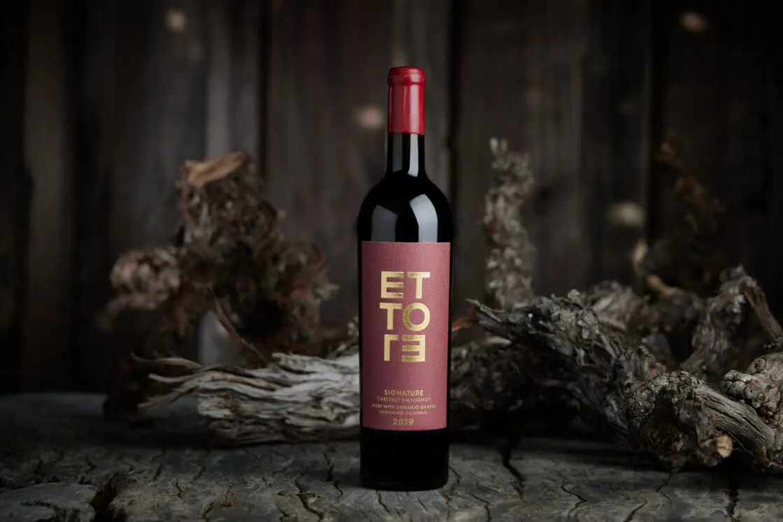 ETTOTE Signature Cabernet Sauvignon wine bottle on rustic wood with blurred background.