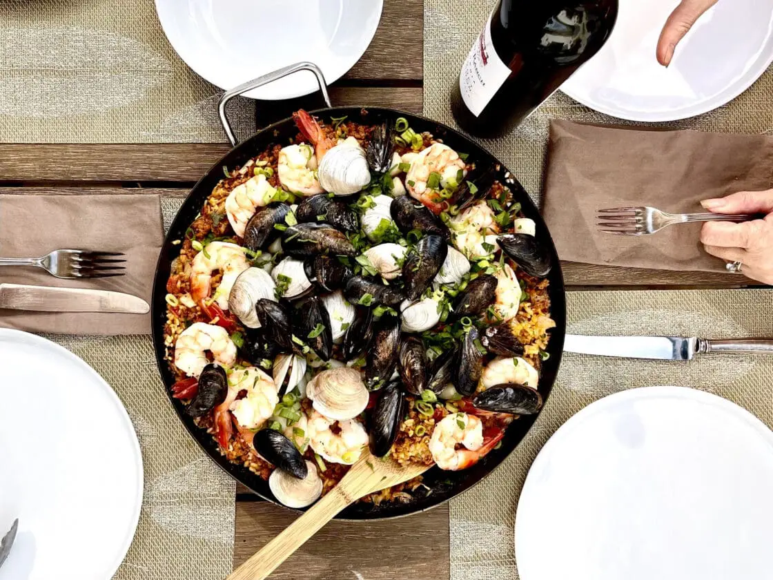 Image of Made In carbon steel paella pan filled with a seafood paella set on a table.