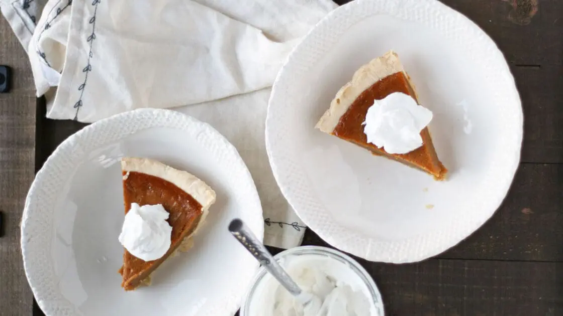 Image of paleo pumpkin pie slices with whip cream on two white plates.