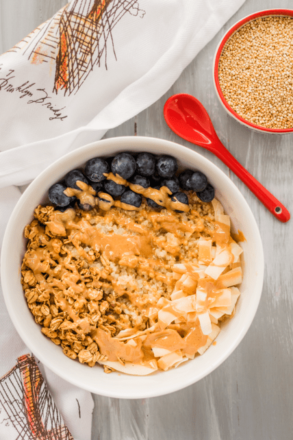 Vegan and gluten-free quinoa breakfast bowl with peanut butter, blueberries, and coconut flakes