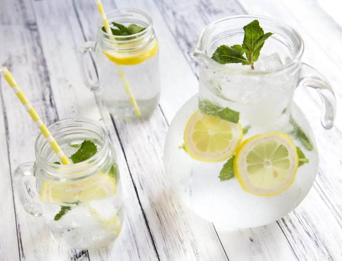 Image of a pitcher of vodka cocktail with sliced lemons and mint, with glasses filled with the same organic sustainable drink for ta boozy brunch.