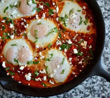 image of Shakshuka recipe, poached eggs in tomato sauce in a cast iron pan on a granite countertop