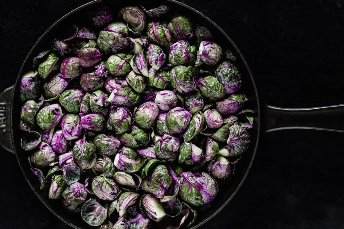 A Staub cast iron skillet filled with gorgeous purple Brussels sprouts.