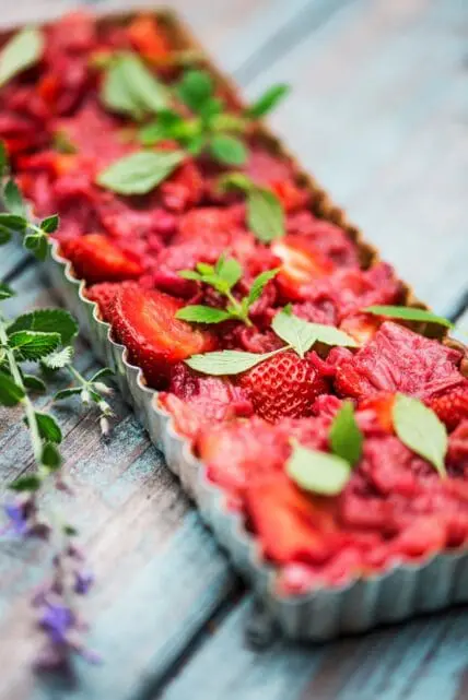 Image of the finished strawberry tart with mint on a wood table with lavender next to tart. This healthy summer tart is perfect to serve at your next BBQ!