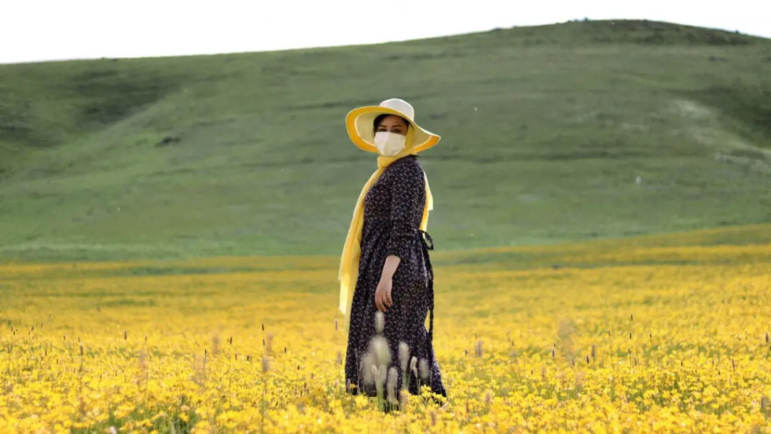 woman standing in field with yellow flowers wearing COVID-19 face mask in Ardabil Privince, Iran