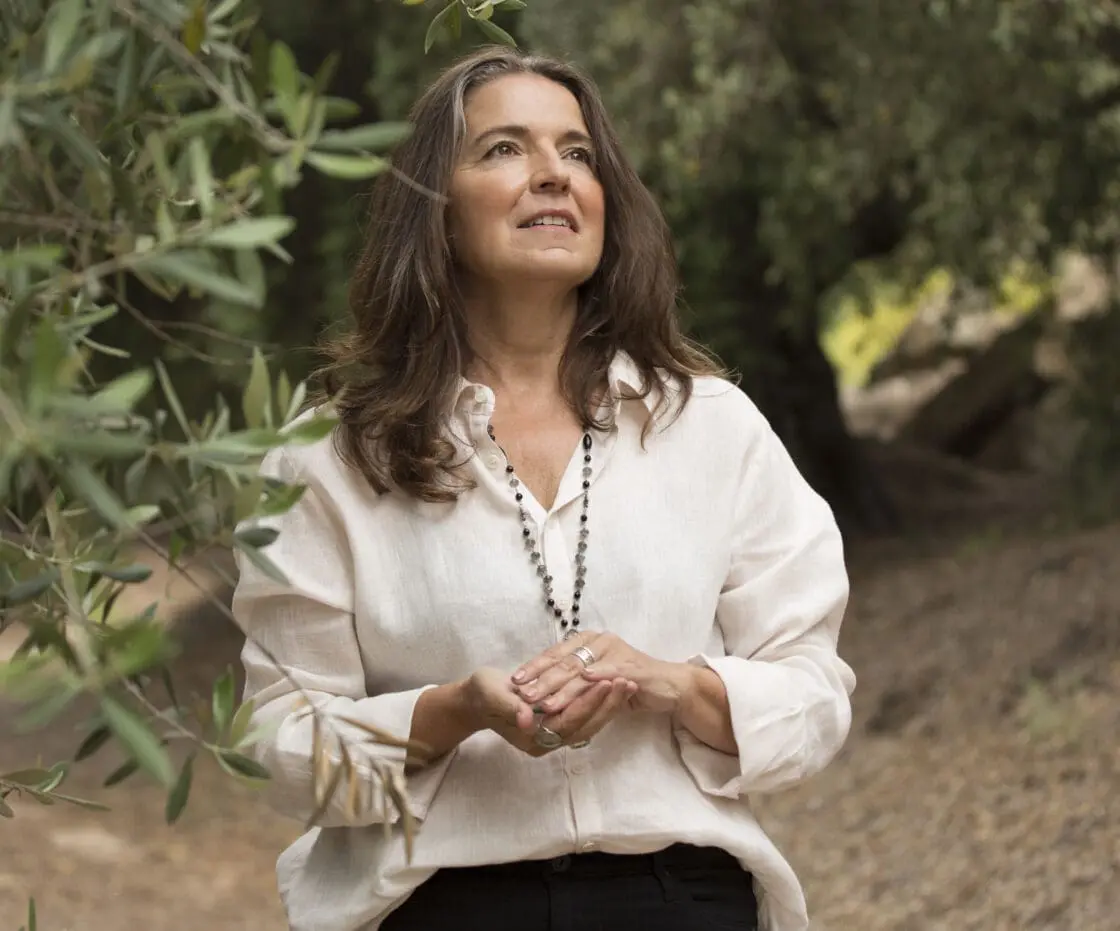 Brunette woman in a white blouse standing among olive tree branches outdoors