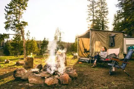 woman sitting next to tent and campfire