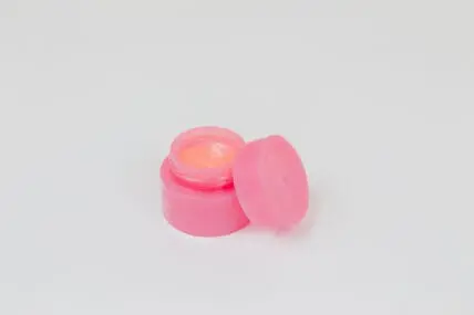 Image of vaseline alternative lip balm in small pink pot with lid set askew showcasing petroleum jelly alternatives.