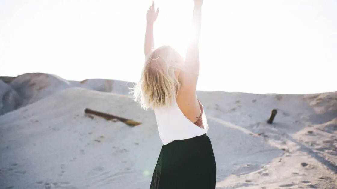 Image of a woman in a desert or beach on the sand reaching her hands towards the sky visualizing what she wishes to manifest.