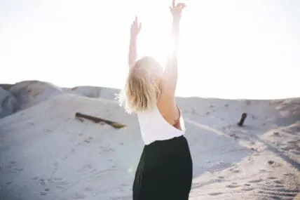 Image of a woman in a desert or beach on the sand reaching her hands towards the sky visualizing what she wishes to manifest.
