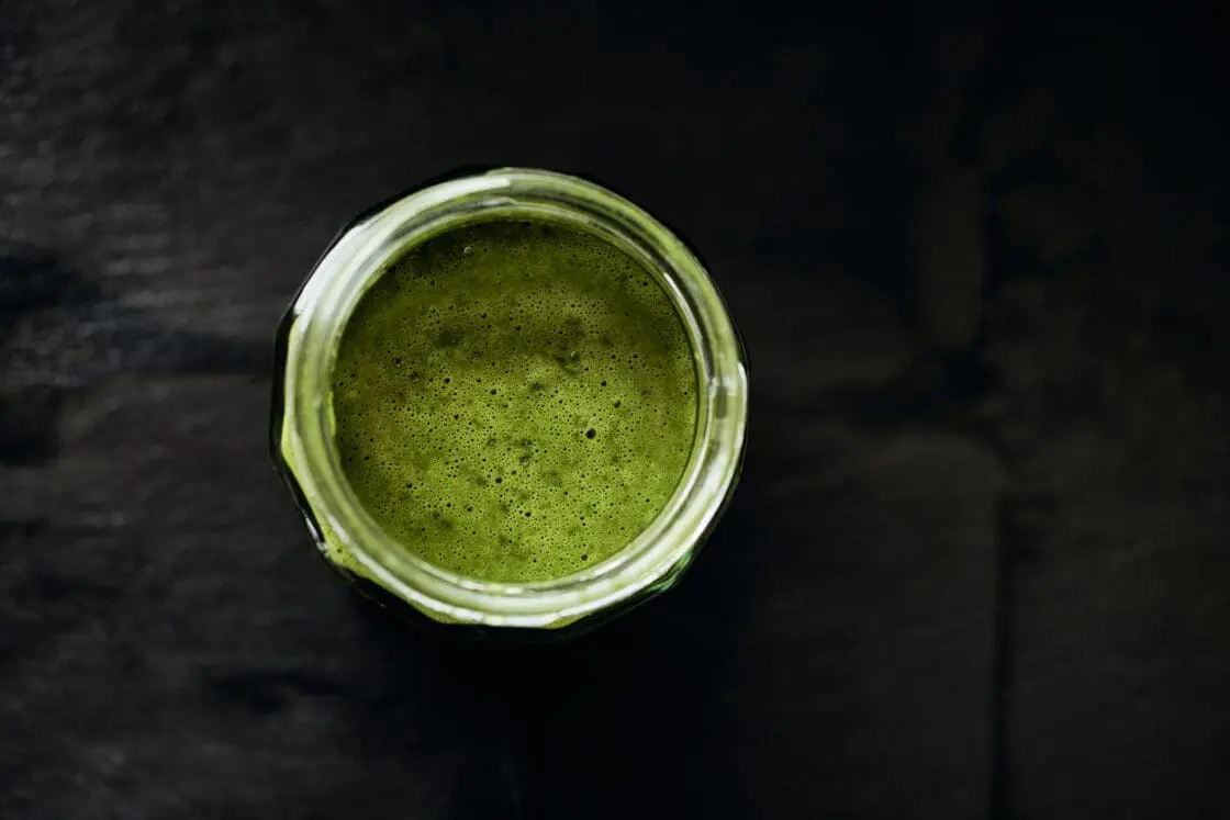 Image of green glass of wheatgrass from wheatgrass powder with black background. Wheatgrass juice is a popular form to take wheatgrass
