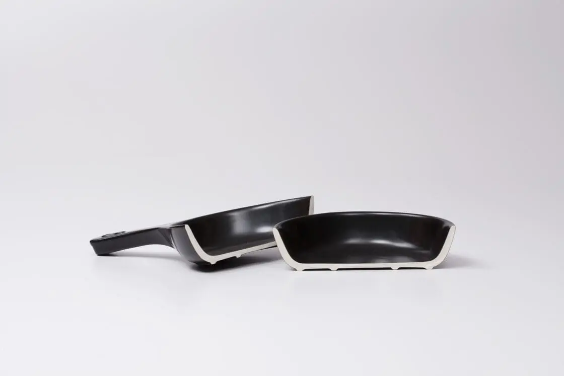Image of a pure ceramic pan cut in half exposing the non-toxic materials, a black exterior with a white interior.