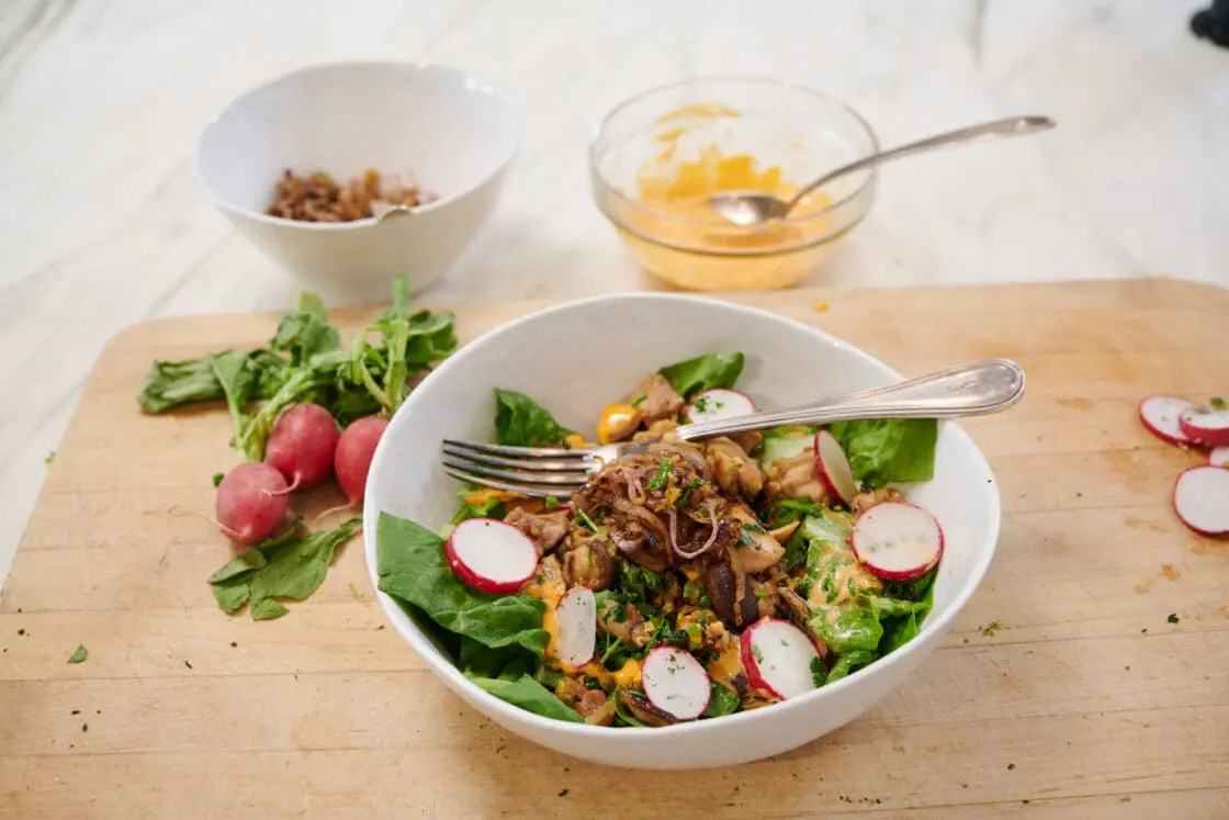 Image of a bowl healthy chicken lettuce bowl recipe with fresh radishes on a wood cutting board. There are two small bowls behind with the crispy shallots and the tangy, creamy, spicy sauce.