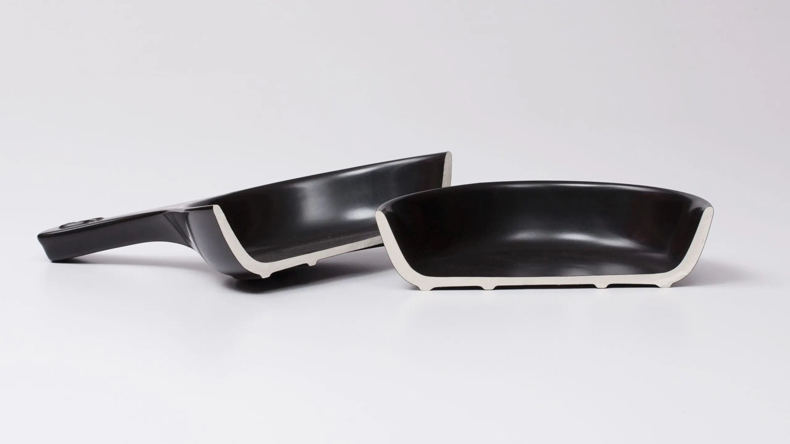 Image of a pure ceramic pan cut in half exposing the non-toxic materials, a black exterior with a white interior.