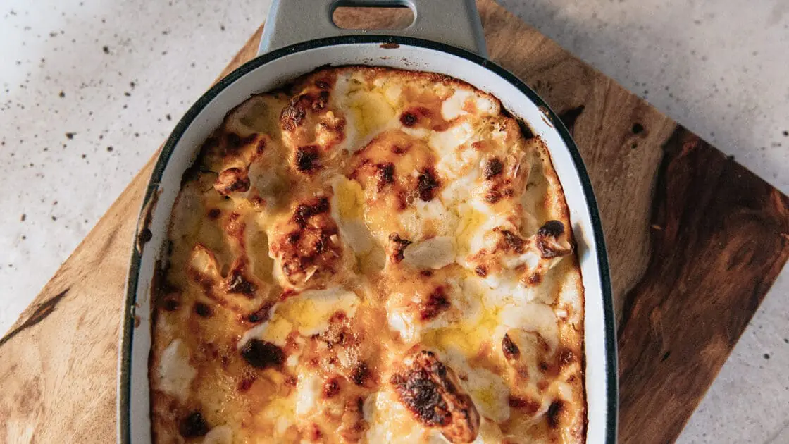 Image of Pampered Chef’s Enameled Cast Iron Baker on a wooden cutting board, filled with cheesy cauliflower and ready to serve.