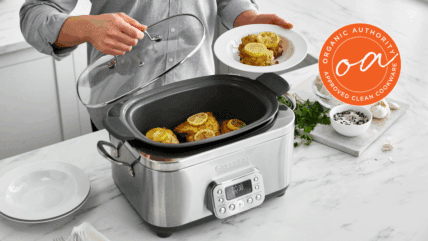 Image of the GreenPan Elite Slow Cooker in Stainless Steel, with a person serving up a chicken dish with lemon slices from the slow cooker.