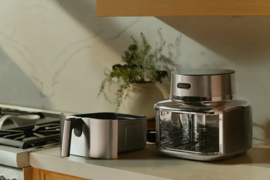 Image of the Cosori Iconic Air Fryer on a marble countertop with the air fryer basket removed and set beside the unit.