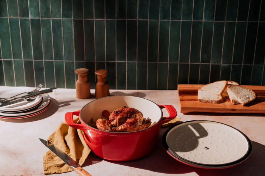 Image of a red cast iron enameled Made In Dutch Oven with a roasted chicken inside.