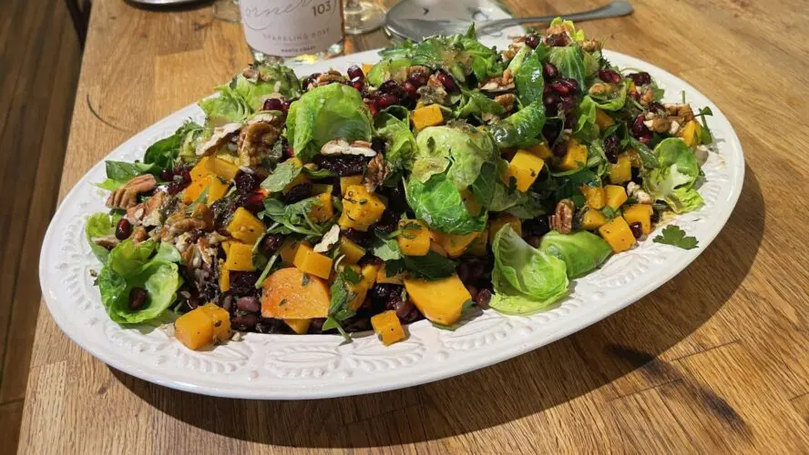 Roasted Brussels sprouts salad with squash, pecans, and dried cranberries on white plate