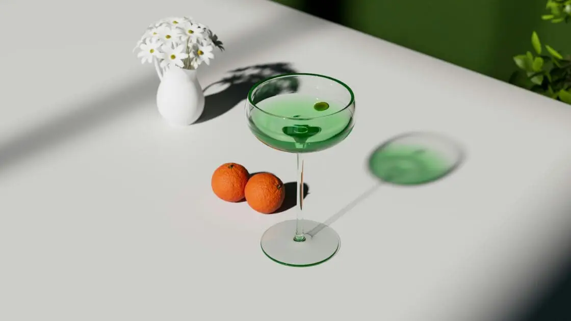 Image of a green cocktail in a coupe glass with two tangerines on the table and a vase of daisies.