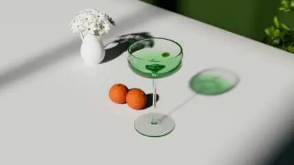 Image of a green cocktail in a coupe glass with two tangerines on the table and a vase of daisies.