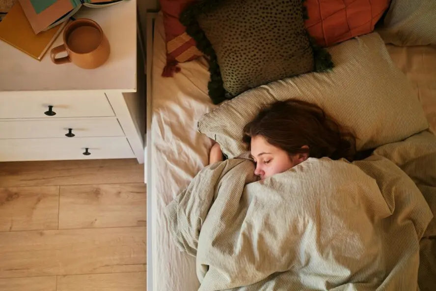Image of a young woman sleeping in bed, with her face half-covered by her duvet.