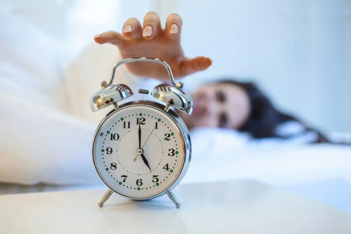 image. of a woman in bed reaching for her alarm clock