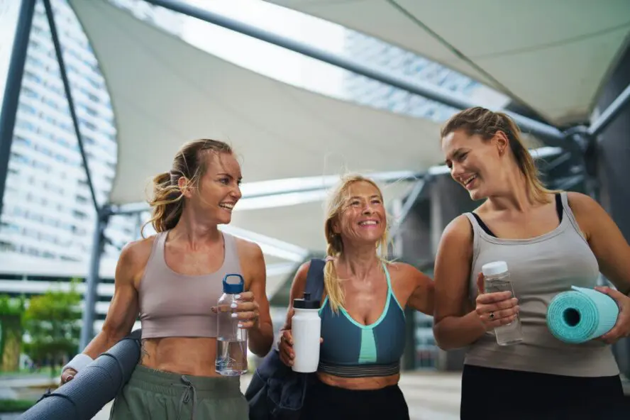 Image of three women holding water bottles and yoga mats after a workout.