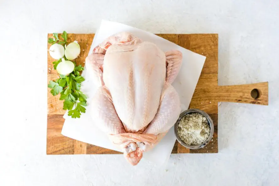 Overhead image of a raw whole chicken under a brick on a wooden cutting board