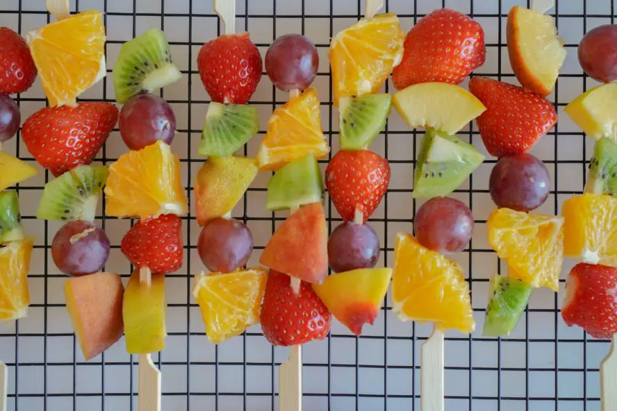 colorful fruit kabobs on a grill with peaches, kiwi, banana, and strawberries before grilling