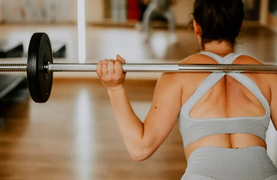 Image of a woman shown from the back with a barbell across her shoulders as she squats.