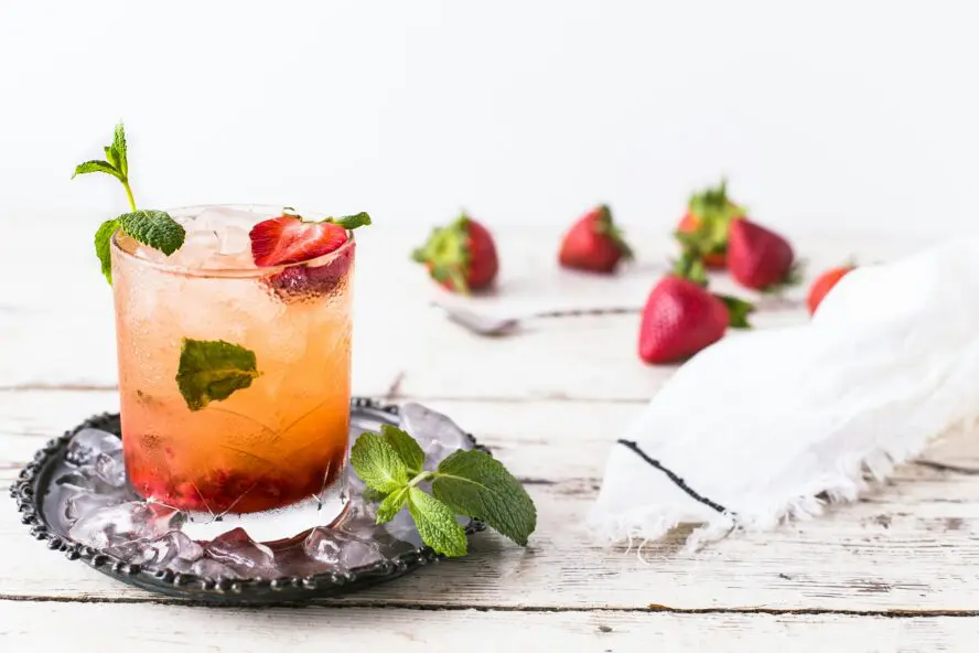 Strawberry Basil Smasher cocktail in a highball glass with a fresh strawberry and basil garnish on an outdoor table