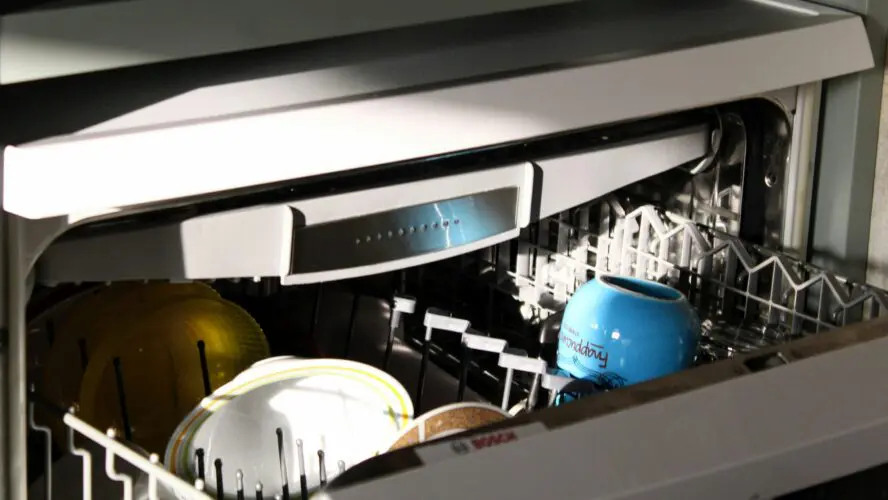 Open dishwasher filled with clean dishes and a blue container of homemade dishwasher soap