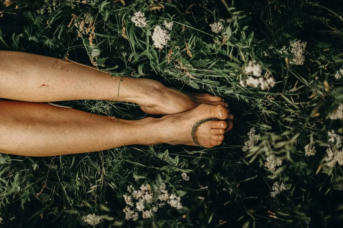 image of a woman's legs and feet in grass and flowers. Showing that touching the earth and being in nature is one answer to "How to reset circadian rhythm"