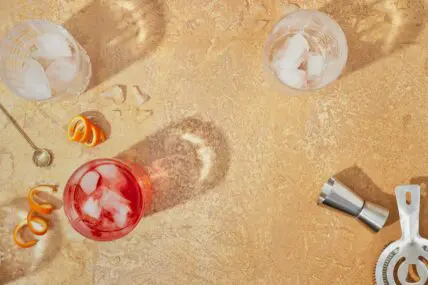 Overhead image of garden-to-glass cocktails arranged on an outdoor concrete surface surrounded by a shaker, glasses of ice, and a jigger