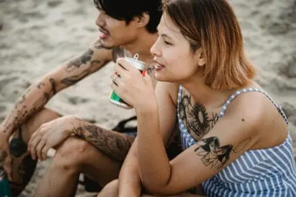 Image of a woman and a man sitting on the beach, sipping probiotic drinks from the can.