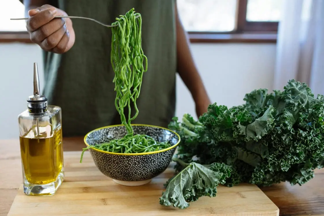 image of the best olive oil for health in a clear bottle with pour spout in front of a bowl of green noodles. What is high phenolic olive oil? or is it the best polyphenol rich olive oil?