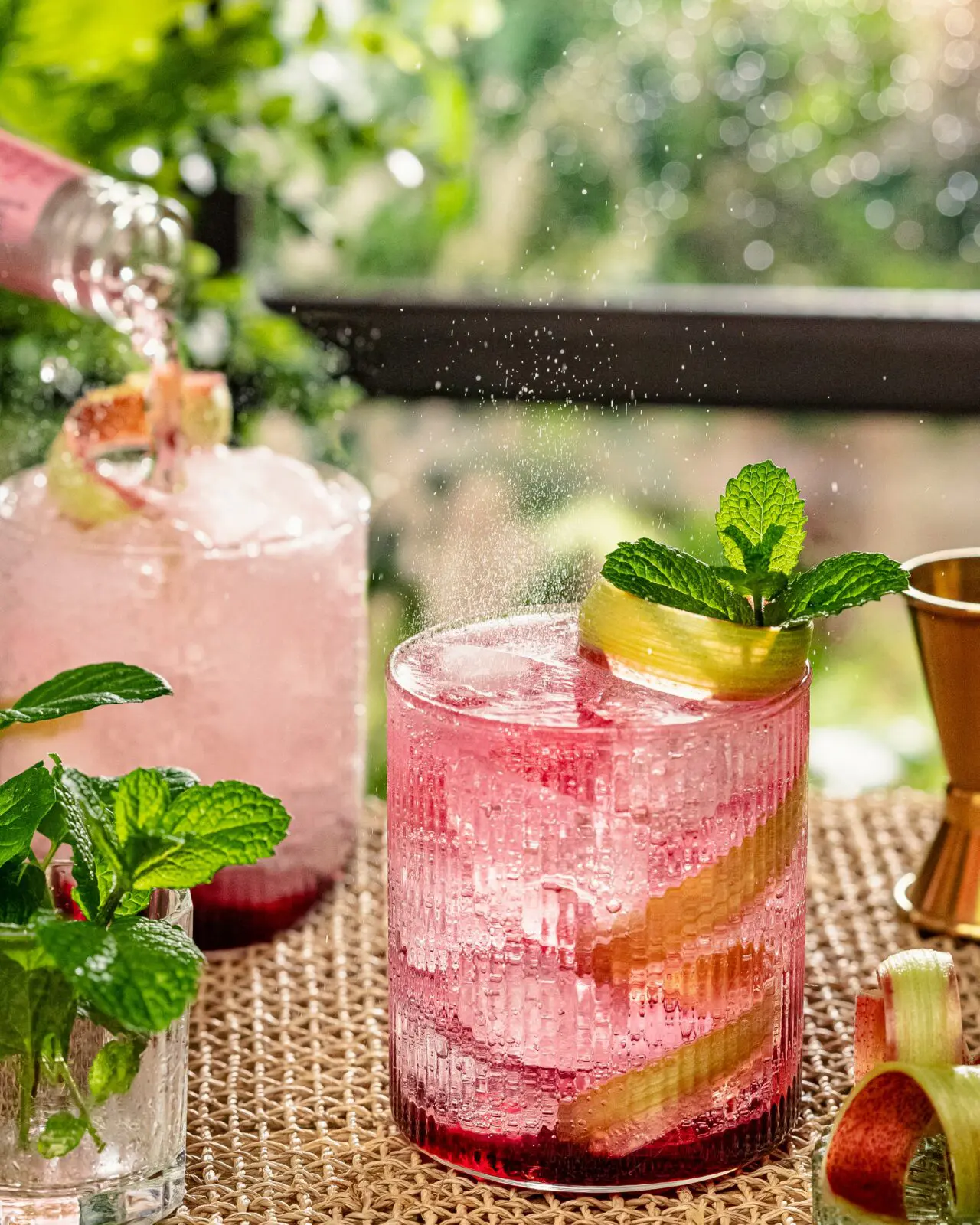 Overhead image of five summer drinks cocktails arranged on an outdoor wooden table surrounded by fresh herbs