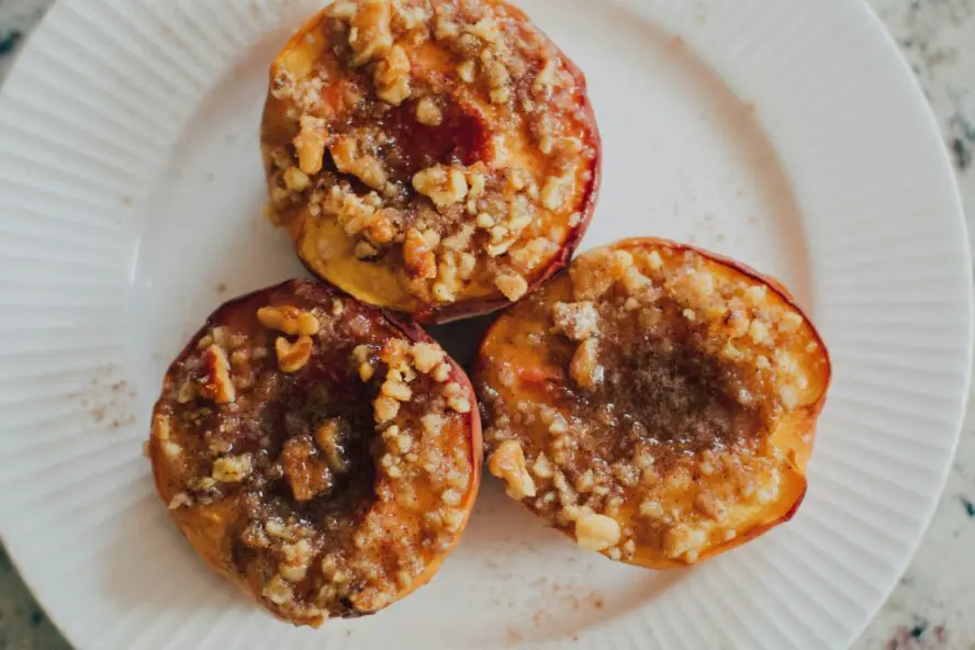 grilled peach halves cut-side up on a white plate showing caramelized grill marks and warm golden flesh topped with granola