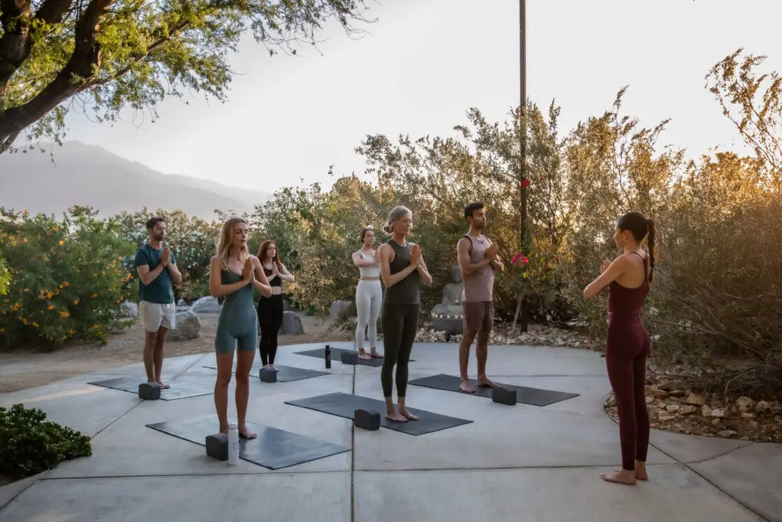 Image of a group of people doing a yoga class outside surrounded by desert and nature.