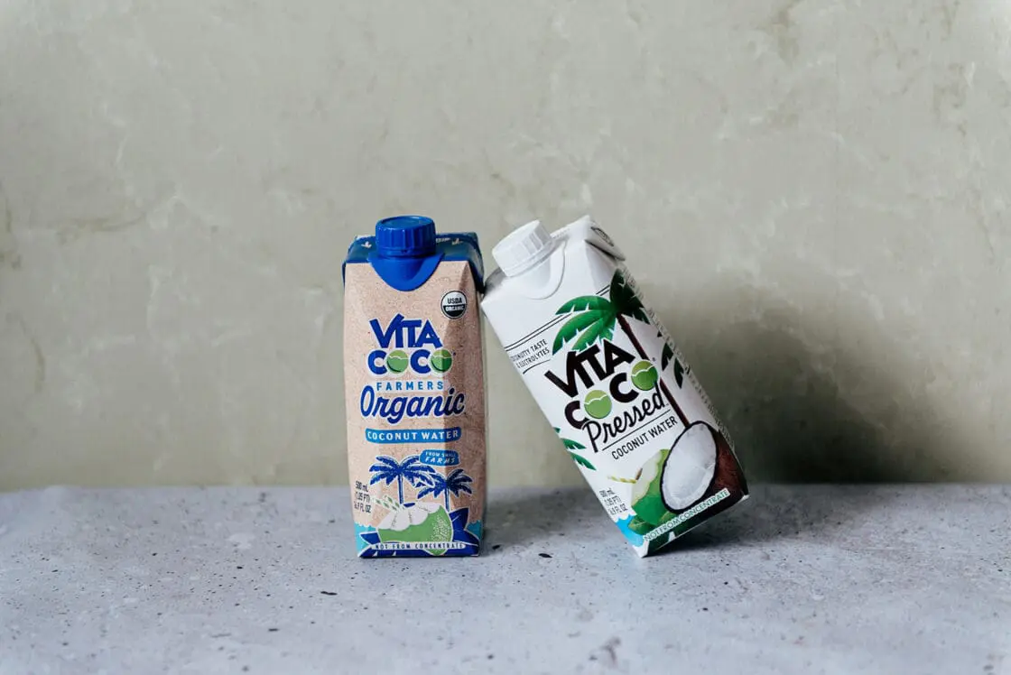 Image of two cartons of Vita Coco coconut water leaning against each other, one is the Farmer's Organic version and the other is the Pressed version.