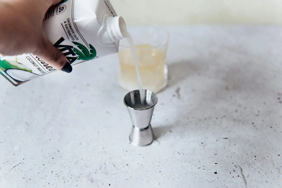 Image of a hand pouring Vita Coco Pressed Coconut Water into a shot to be used in a coconut water drink recipe.